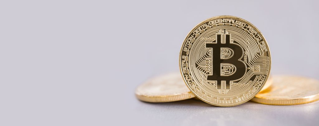 Inversió Jove 2 Primer pla d'una moneda física de Bitcoin sobre un fons clar, amb altres monedes desenfocades al darrere.